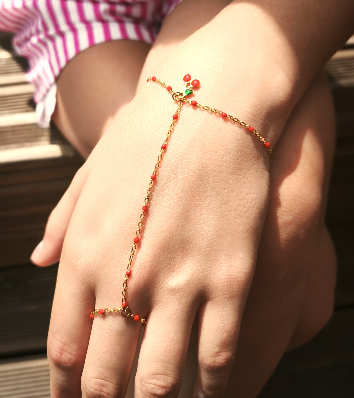 bracelet en acier inoxydable et perle rouge. bracelet de main avec une pampille cerise très moderne pour l'été